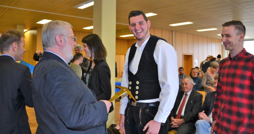 33 Teilnehmer, 32, die sich der Prüfung stellten, davon 4 Damen und eine Erfolgsquote von 93,75 %: Das sind die reinen Zahlen des Vorbereitungslehrgangs auf die Gesellenprüfung im Dachdeckerhandwerk 2019. Dahinter stecken Erwartungen, Hoffnungen und individuelle Lebensläufe, die nun eine wichtige Wegmarke erreicht haben.Denn jetzt gilt: „Ich bin Dachdecker – ich kann das!“ Mit diesem Ausruf, den Artur Wierschem, Geschäftsführer des BBZ Mayen, in seiner Begrüßung anlässlich der Freisprechungsfeier am 27.04.2019 im Bundesbildungszentrum des Deutschen Dachdeckerhandwerks den erfolgreichen neuen Gesellinnen und Gesellen in den Mund legte, ist all das verbunden, was in knapp 4 Monaten erreicht wurde.Eine fachliche Qualifikation, eine Steigerung des eigenen „Marktwertes“ aber auch nicht zuletzt Stolz und ein gestärktes Selbstbewusstsein, verbunden mit der Liebe zum Dachdeckerhandwerk. Zahlreiche Ehrengäste erwiesen gemeinsam mit den Freunden und Verwandten sowie den Ausbildern des BBZ den AbsolventInnen die Ehre. Rolf Schumacher, Bürgermeister der Stadt Mayen, Michael Zimmermann, Vizepräsident des ZVDH, Peter Hahn, operativer Geschäftsführer der ARGE Koblenz-Mayen sowie Ulrich Sparrer, Vorsitzender des Berufsbildungswerks des Deutschen Dachdeckerhandwerks gratulierten zum Erfolg.„Mein Glückwunsch dazu, in eine Währung investiert zu haben, die keine Grenzen und keine Inflation kennt, in die eigene Ausbildung“, so Michael Zimmermann. „Sie sind der 50. Jahrgang, also sozusagen ein goldener Jahrgang“ begrüßte der Landesinnungsmeister des rheinland-pfälzischen Dachdeckerhandwerks die Gesellinnen und Gesellen und betonte die Bedeutung dieses Lehrgangs, der die Möglichkeit des „Quereinstiegs“ bietet und der in der Regel, so Lauer, von „Überzeugungstätern“ gewählt wird, von Menschen die den festen Willen haben, dem Dachdeckerhandwerk treu zu bleiben. Die Besten der 30 Teilnehmer: 1. Tobias Skoruppa aus Rheinböllen, Rheinland-Pfalz, mit 91,3 Punkten,2. Eduard Kelsch aus Göllheim, Rheinland-Pfalz, mit 88,8 Punkten und 3. Sebastian Schmitt aus Sailauf, Bayern, mit 85,1 Punkten Der nächste Kurs startet am 06.01.2020.